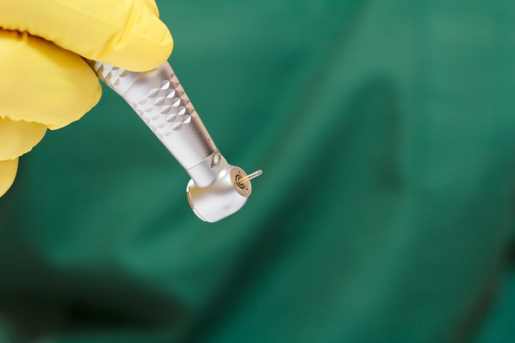 Dental handpiece held in a yellow glove against a green background
