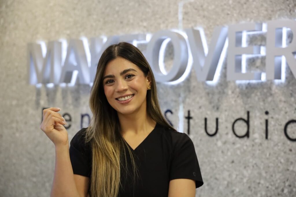 Team member smiling beside the Makeover Dental Studio sign in Tijuana