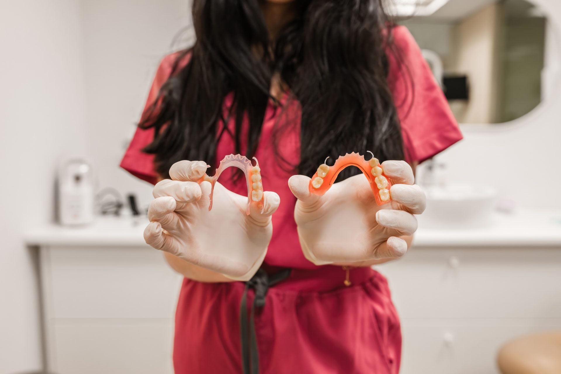 Dental professional in red scrubs holding two removable partial dentures