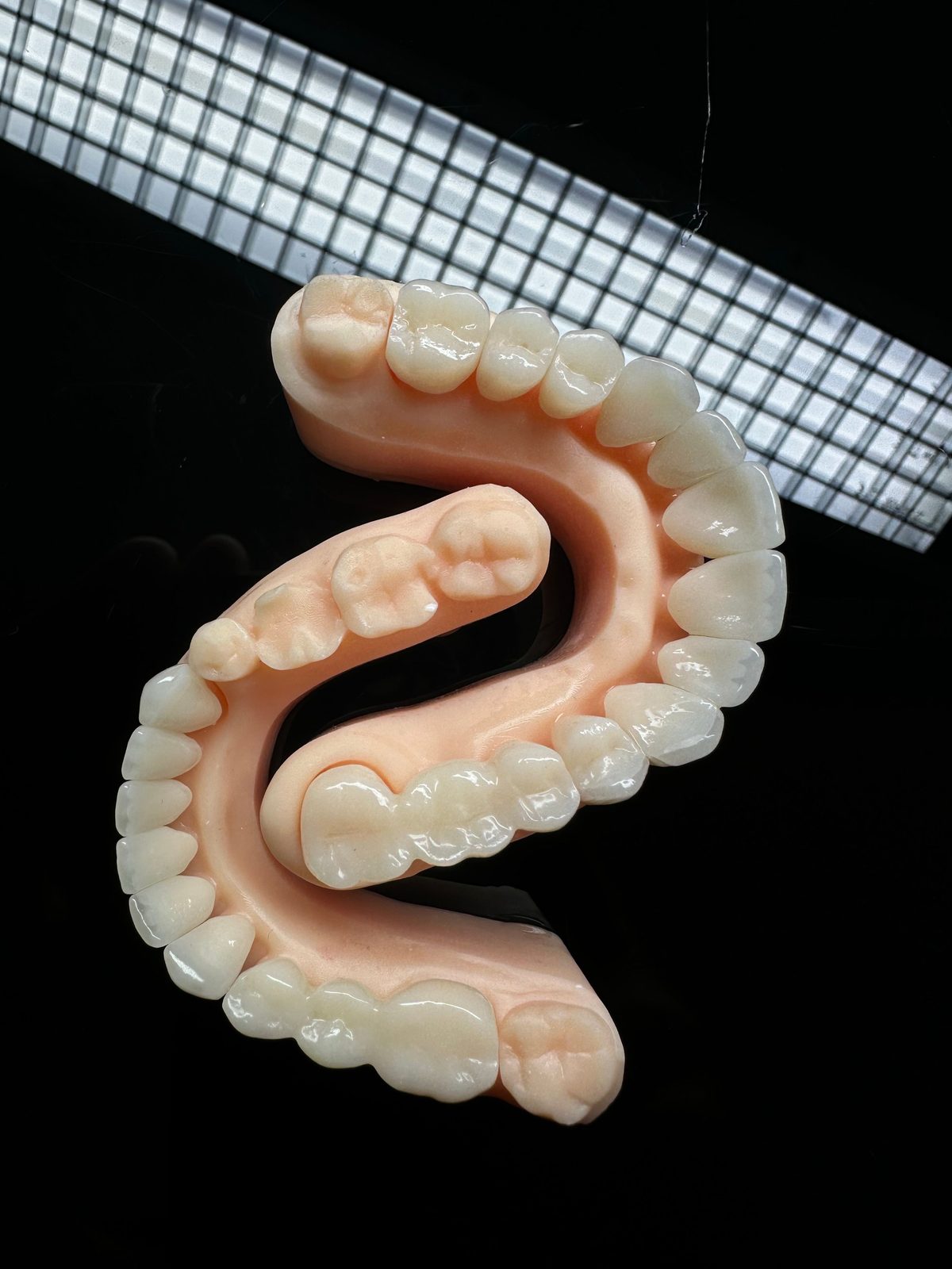 Milled zirconia denture arch resting on a checkered work surface